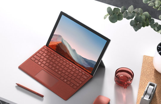A Surface Pro 7 with a poppy red Type Cover, a Pen and an Arc Mouse on a desk.