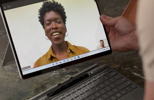 A person holds a Surface Pro X which features the smiling face of another person.
