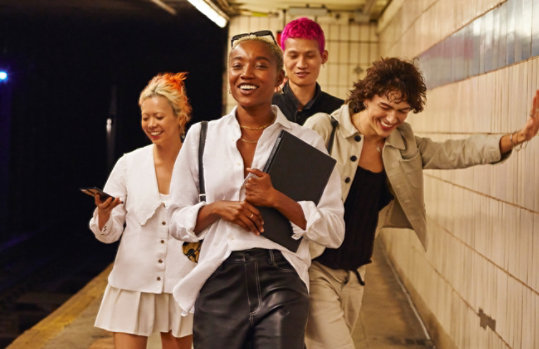 A group of young people on a metro platform. One girl is looking at a smart phone.