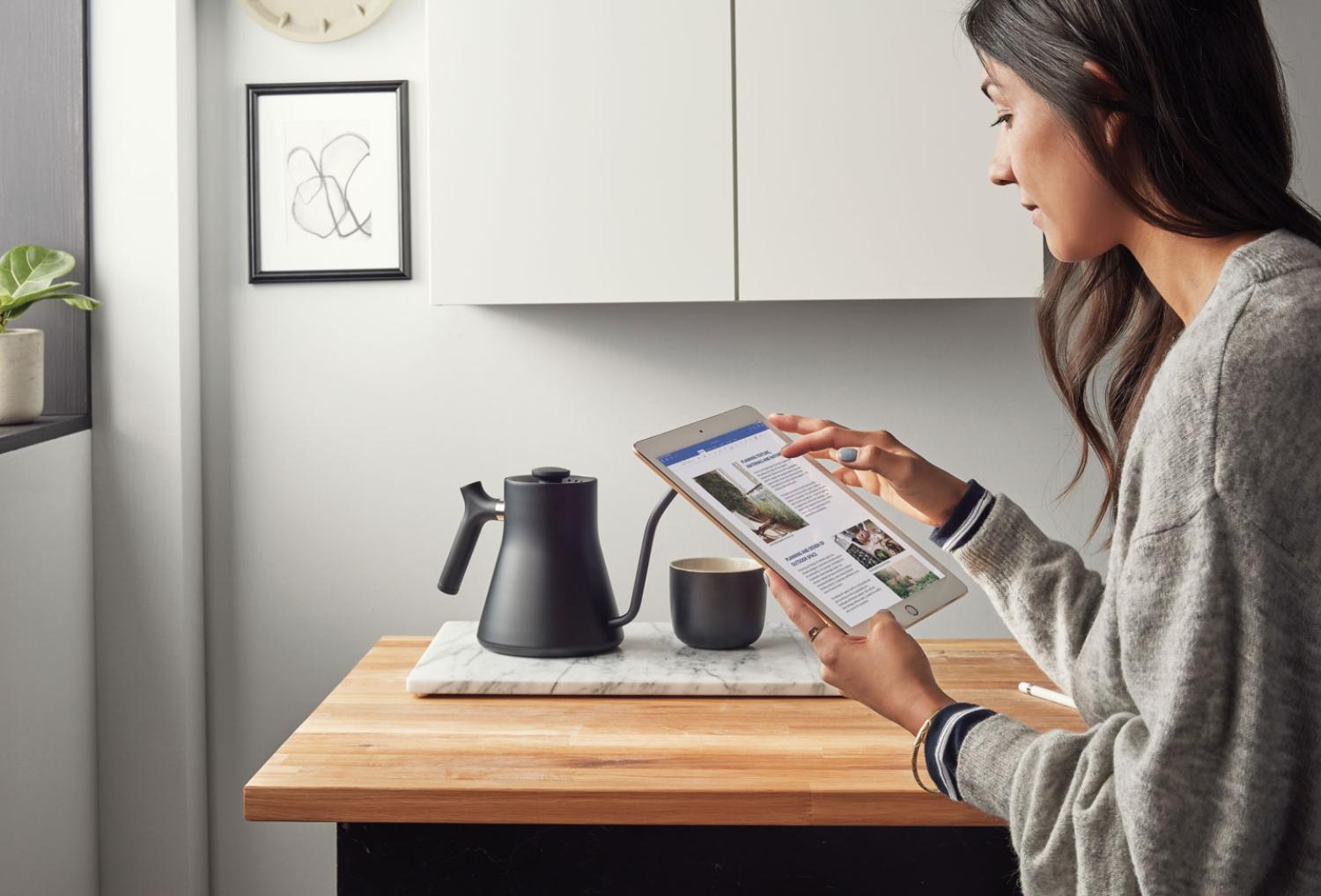 Person using an iPad with a stylus while seated at a table in a casual environment