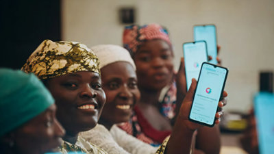A group of smiling women hold up smartphones displaying an app.