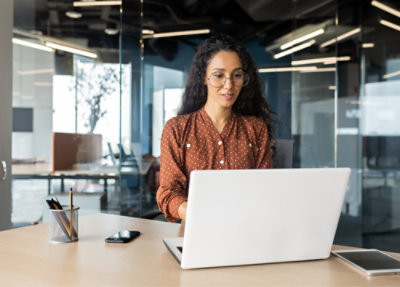 A woman in a polka dot shirt working on a laptop in a modern office setting.