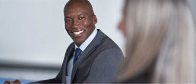 A smiling Black man in a business suit sitting at a table across from a woman with blonde hair