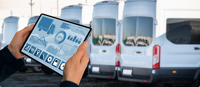 Person holding a tablet displaying fleet management software in front of a row of parked white delivery vans.