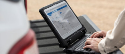 A man using a laptop on the back of a truck.