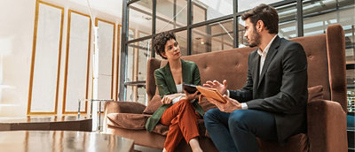 A businesswoman and businessman speaking together while sitting down.