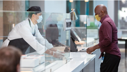 A café worker wearing a mask and gloves assisting a customer