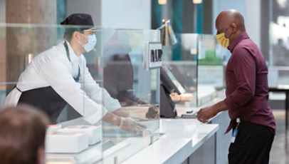 En cafemedarbejder har mundbind og handsker på, mens denne assisterer en kunde