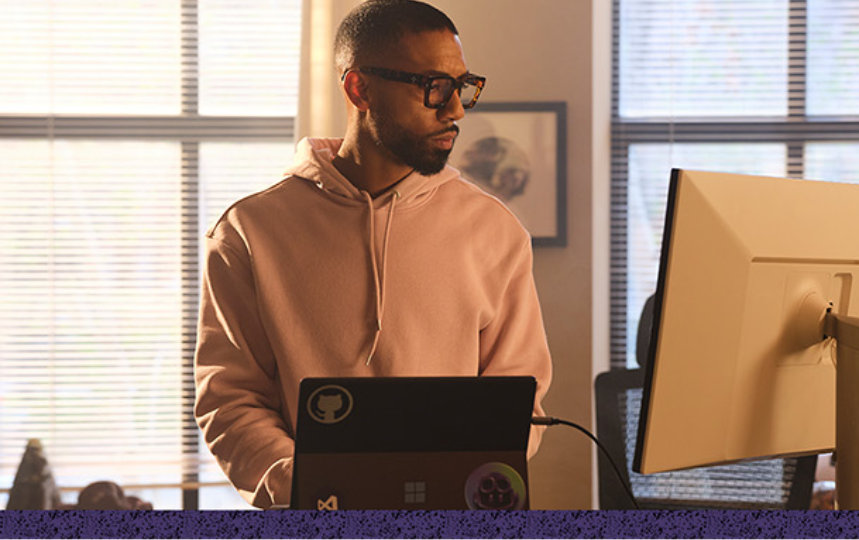 Man typing on a laptop in front of him and looking at a monitor on his left