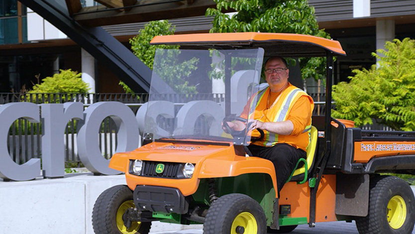 Jason Lakey is driving an orange 'gator' four wheeled vehicle. He is dressed in orange and a high-visibility vest. Behind the gator is a large Microsoft sign.