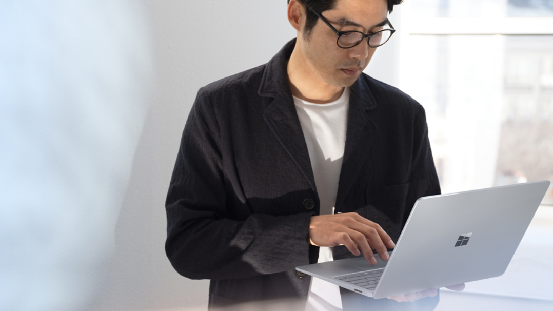Man wearing a black jacket holding a Windows laptop
