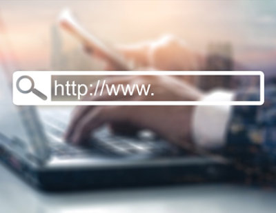 A hand typing on a laptop with a blurred image in the background.