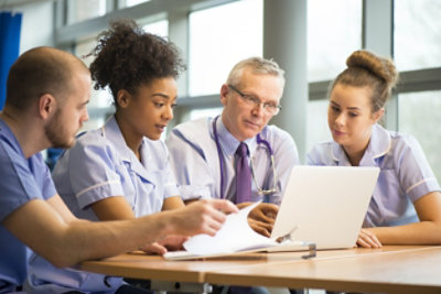 Eine Frau in einem weißen Laborkittel spricht mit zwei Männern, während sie ein Tablet verwendet.