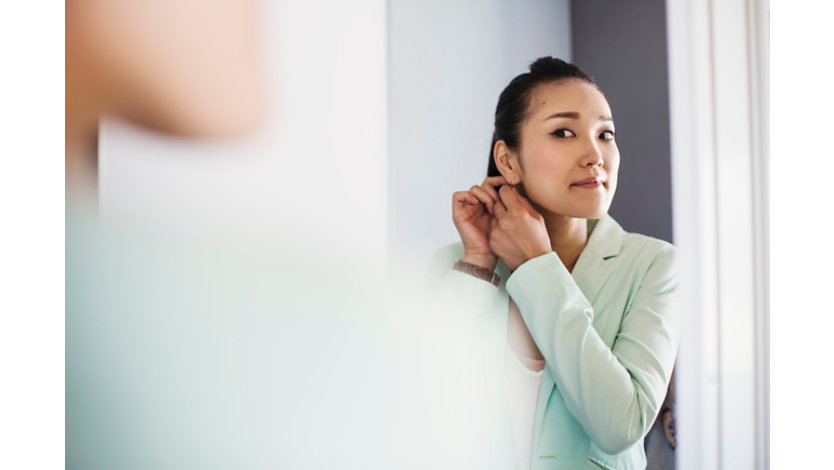 Person adjusting an earring while looking into a mirror, preparing for the day in an indoor setting.