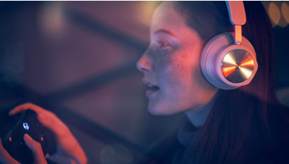 A person wearing Beoplay Portal Headphones and holding an Xbox controller.