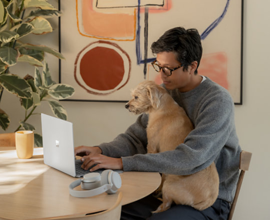 A man types on his laptop while working at home with his dog.