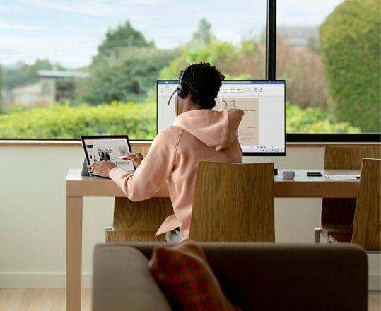 Een student werkend aan zijn bureau met Office-apps op een laptop met aparte monitor.