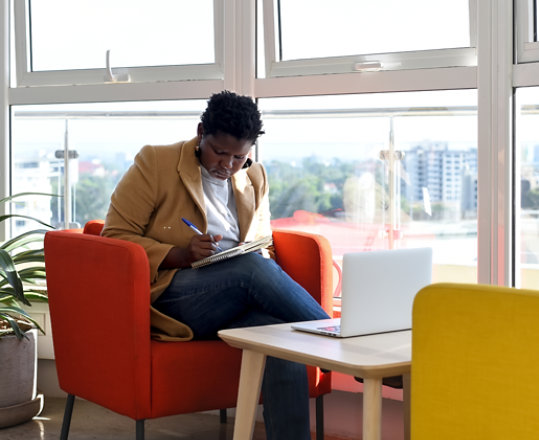 Una mujer toma notas sentada con su portátil en una oficina moderna.