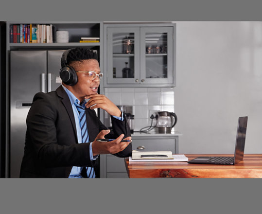 A person wearing a suit and tie uses a laptop while sitting in a kitchen.