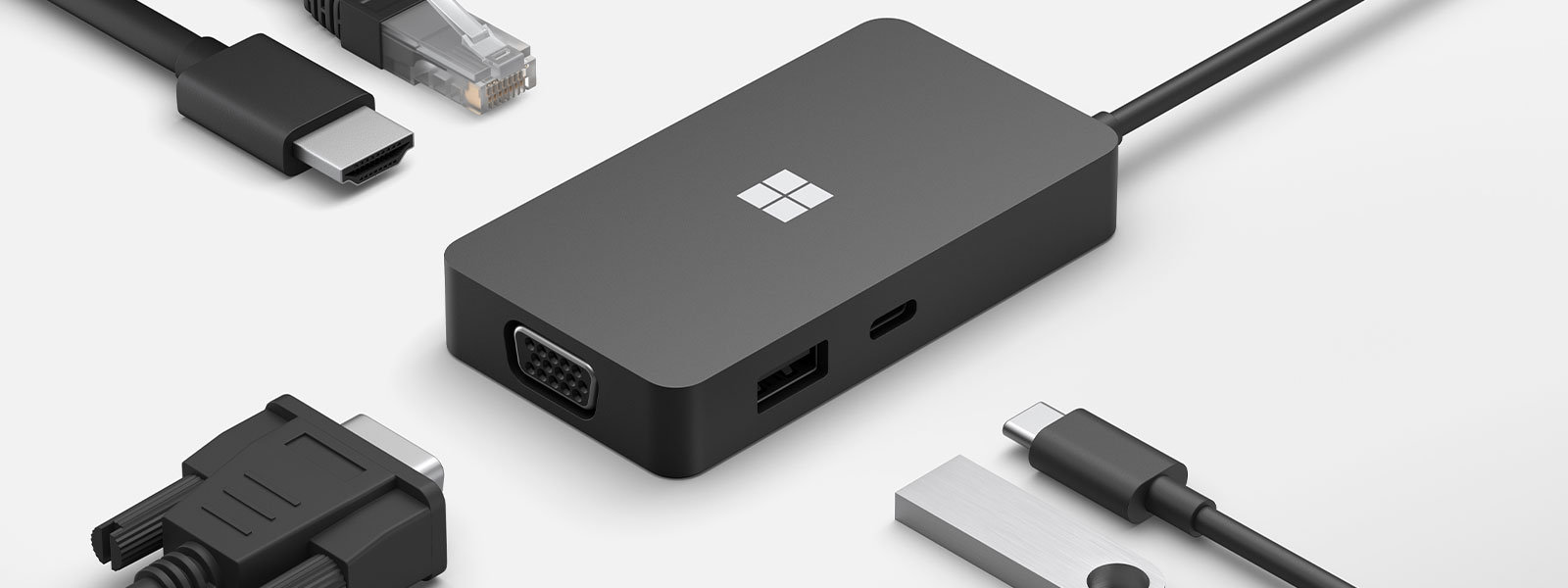 A Microsoft USB-C® Travel Hub with multiple cable connections displayed around it’s ports