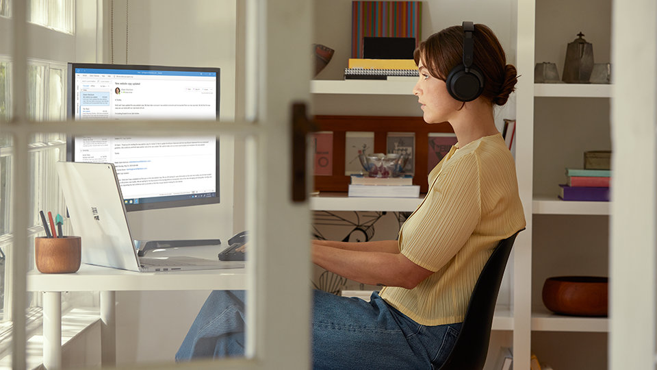 Une personne portant un casque Surface Headphones+, assise au bureau en regardant un écran d’ordinateur.