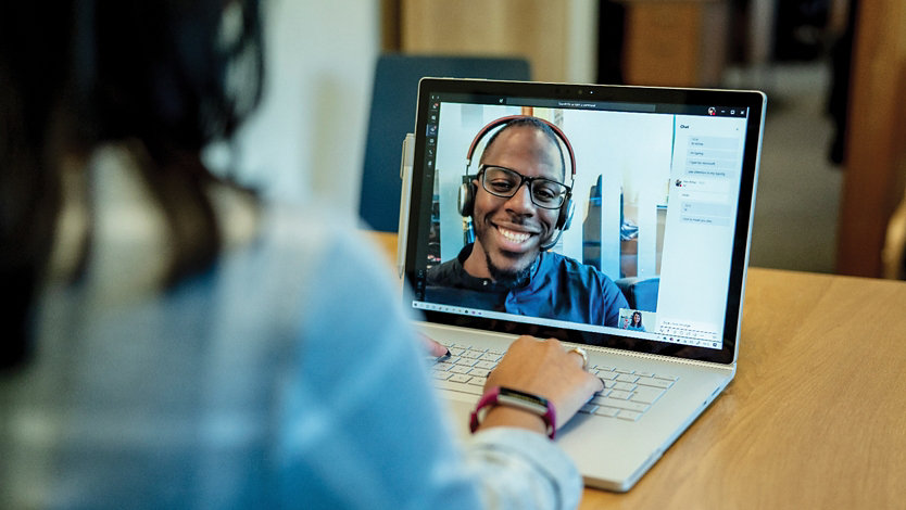 Two people talking via teams, one on the screen, and sitting at a desk.