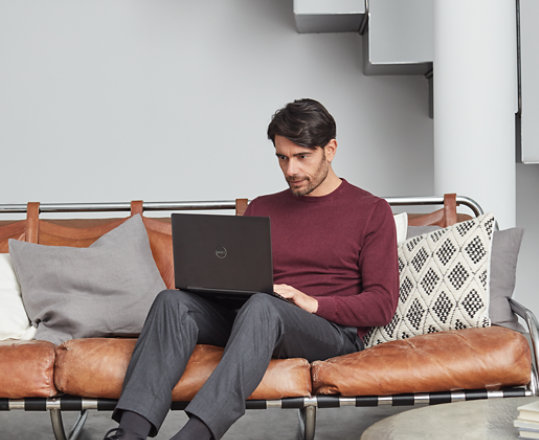 A person using Visio on his Surface laptop while sitting on a leather sofa with pillows.