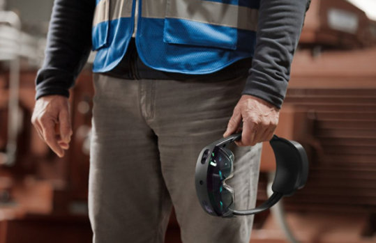 A person holds a HoloLens 2 device at their side.