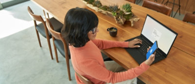 A woman is working on a laptop with a phone in hand