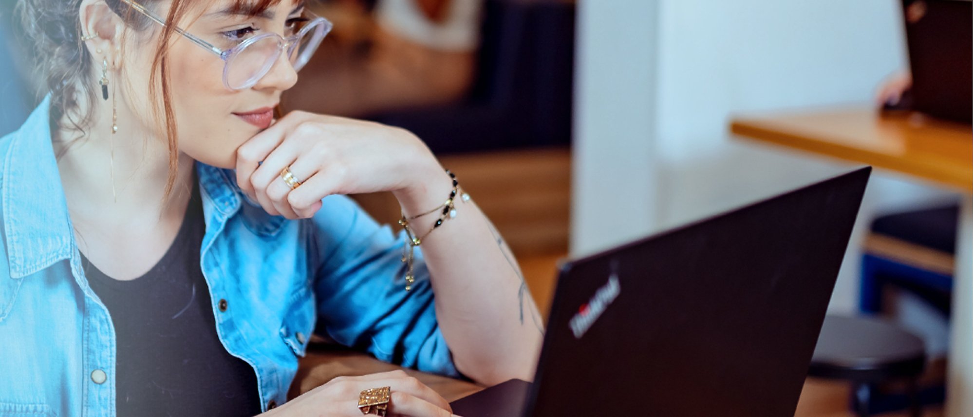 Eine Frau mit Brille arbeitet mit einer Hand auf dem Kinn an ihrem Laptop
