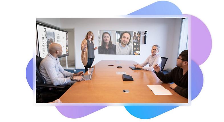 Quatro pessoas numa sala de reuniões e uma chamada de vídeo do Teams com colunas inteligentes instaladas numa parede atrás das mesmas.