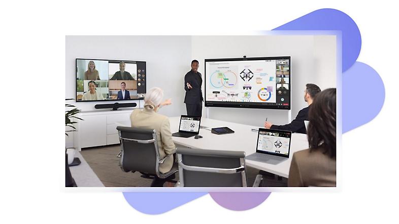 Four people in a meeting room with two large screens displaying a presentation and a Teams video call and laptops and a Sennheiser TeamConnect Intelligent Speaker device on the table.