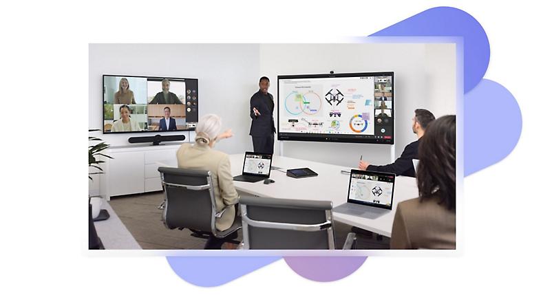 Fire personer i et møderum med to store skærme, der viser en præsentation og et Teams-videoopkald og bærbare computere og en Sennheiser TeamConnect Intelligent Speaker-enhed på bordet.