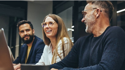 Several people smiling and working together on laptops in an office