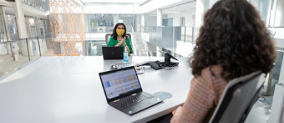 Una persona con la mascherina è seduta alla scrivania con un portatile e un flacone igienizzante in un ufficio moderno.