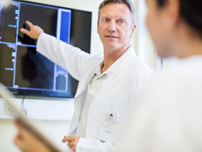 A man in a white coat pointing at a screen.