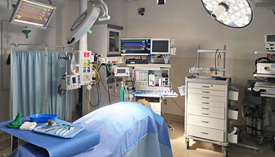 A hospital room with medical equipment, a white drawer, and a blue curtain.