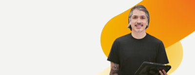 A person with grey hair holds a tablet and smiles, standing against a white background 