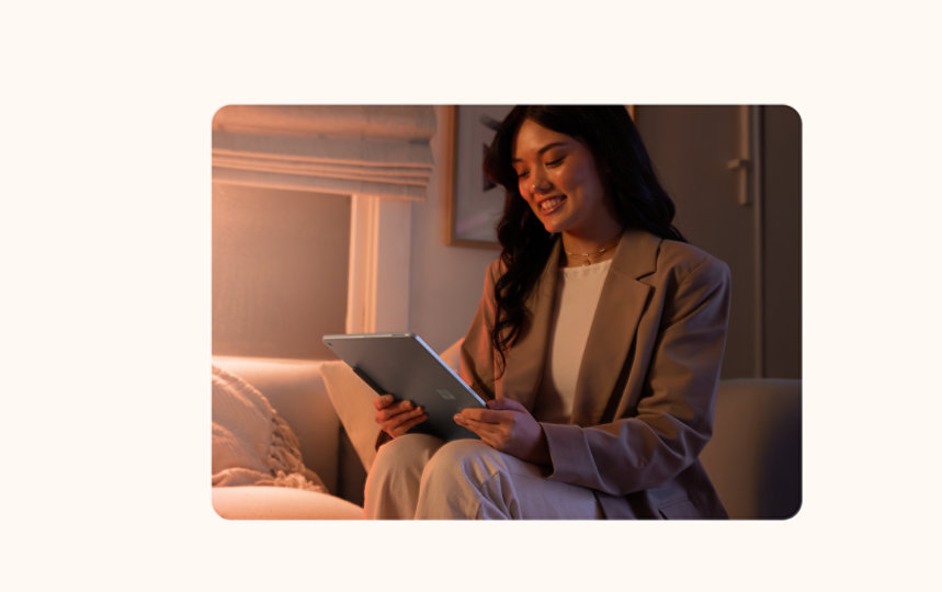 暖かな照明の部屋で、ソファに座りマイクロソフト・サーフェス・プロのタブレットを使用している女性。