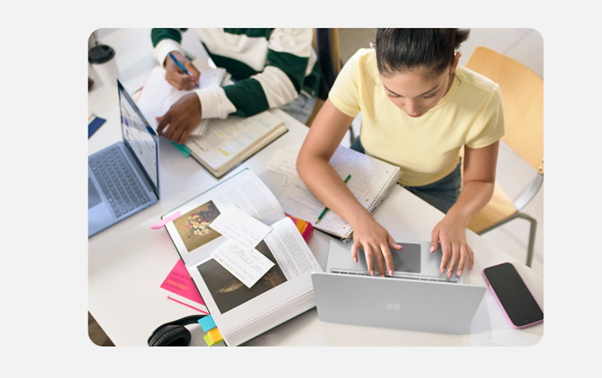 Büyük bir masada oturan ve Surface Laptop cihazlarını kullanarak bir proje üzerinde birlikte çalışan üç üniversite öğrencisi.