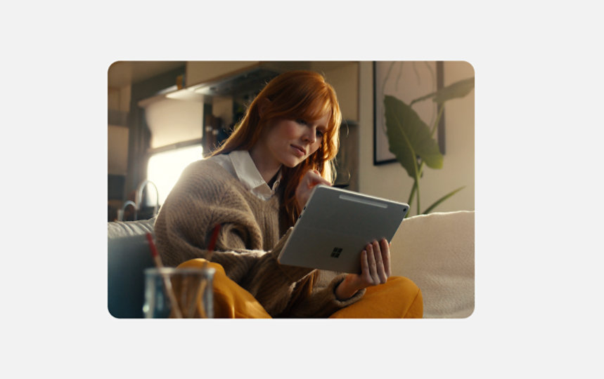 Teacher sitting on a couch using a Surface Pro in Platinum in a home office.