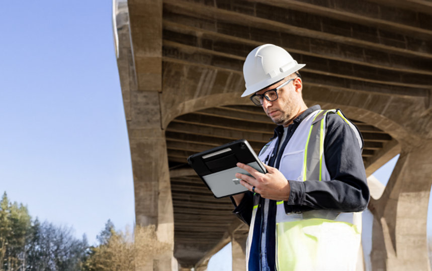 ベストを着てヘルメットをかぶり、Surface Pro 12を持っている男性の写真。