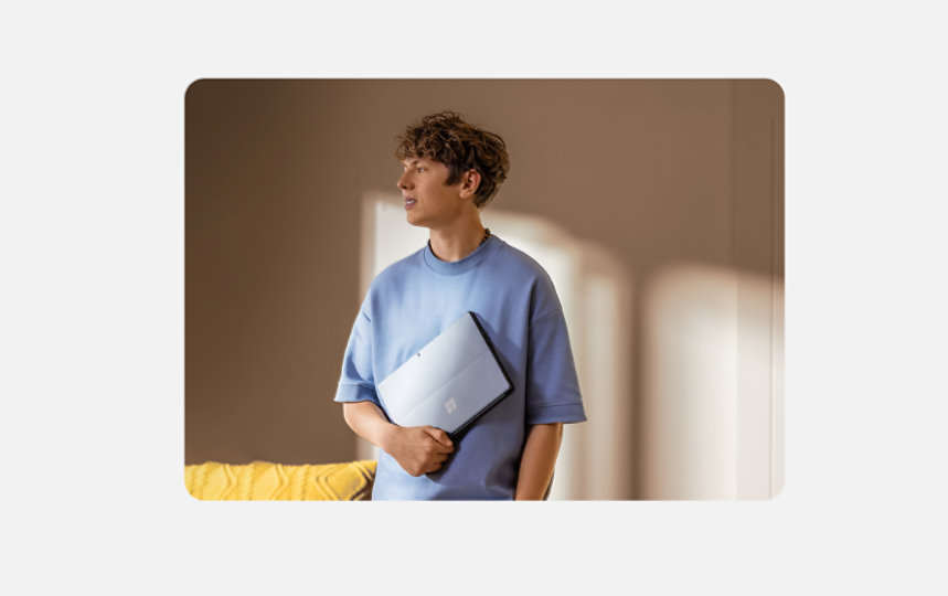 Person standing in a room beside a sofa, holding a Surface Pro in their arm.