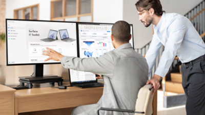 Two professionals discussing data on a dual monitor setup in a modern office.