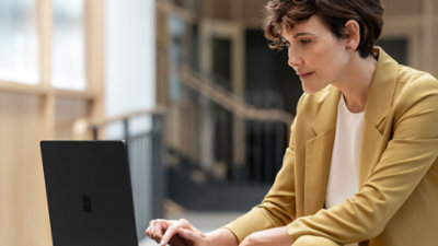 A woman sitting while working on a Black Surface Laptop.