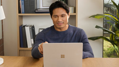 A man sitting at a desk using a Platinum Surface Laptop.
