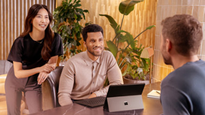 An adult male using Surface Pro (11th edition) Copilot+ PC with another adult male and female inside indoor setting.