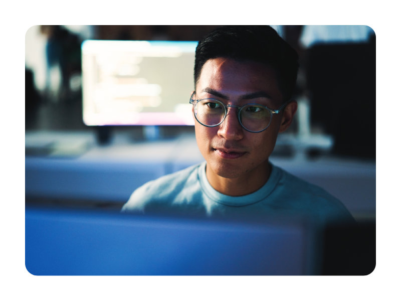 Person focused on a computer workstation in a modern office environment with multiple screens in the background.