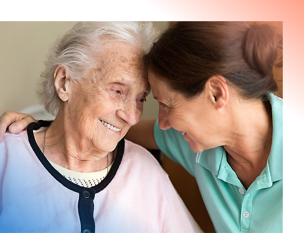 A smiling elderly woman with white hair receives a loving embrace from a middle-aged woman, both looking joyful.