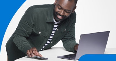 Personne penchée au-dessus d’une table utilisant un ordinateur portable et un téléphone mobile.